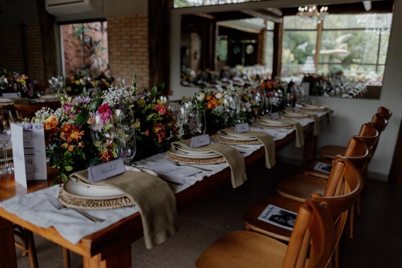 Mesa longa com cadeiras de madeira e arranjo floral central