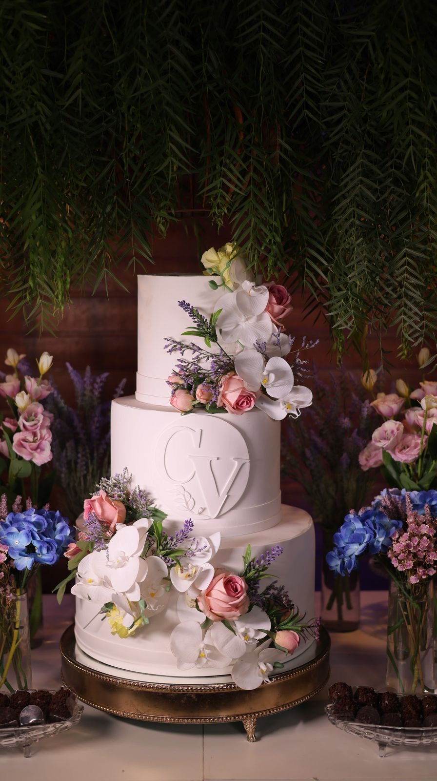 Mesa de doces com bolo de três andares e flores em tons de coral